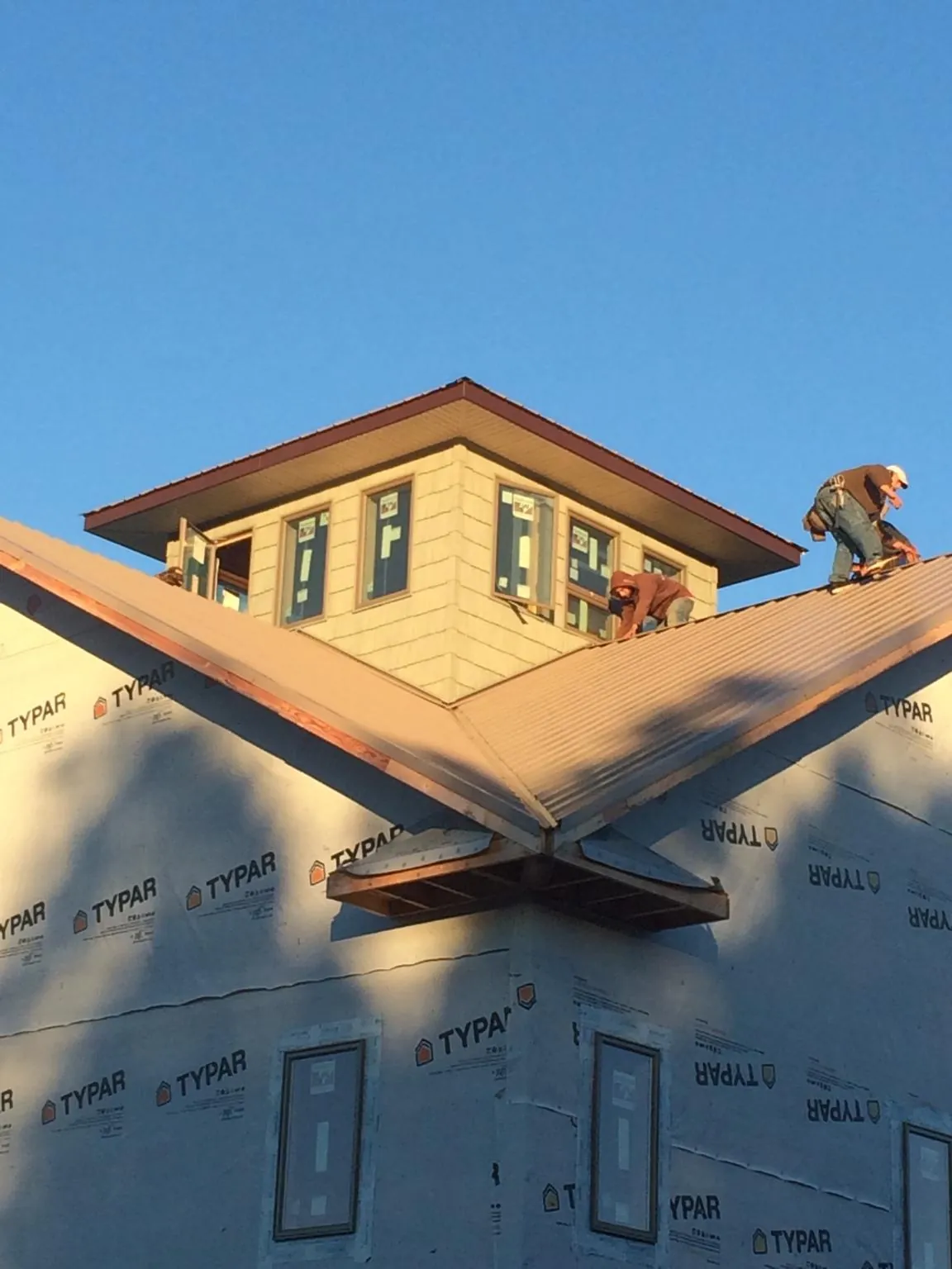 Roofers working around a rooftop cupola on a new metal roof at sunset — Roof Waterproofing in Groton by Roofing Brothers